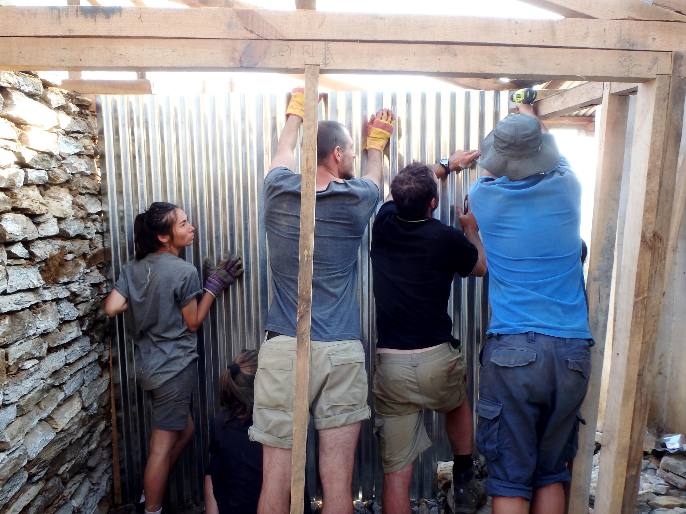 A group of construction volunteers fixing metal sheeting to a basic timber frame