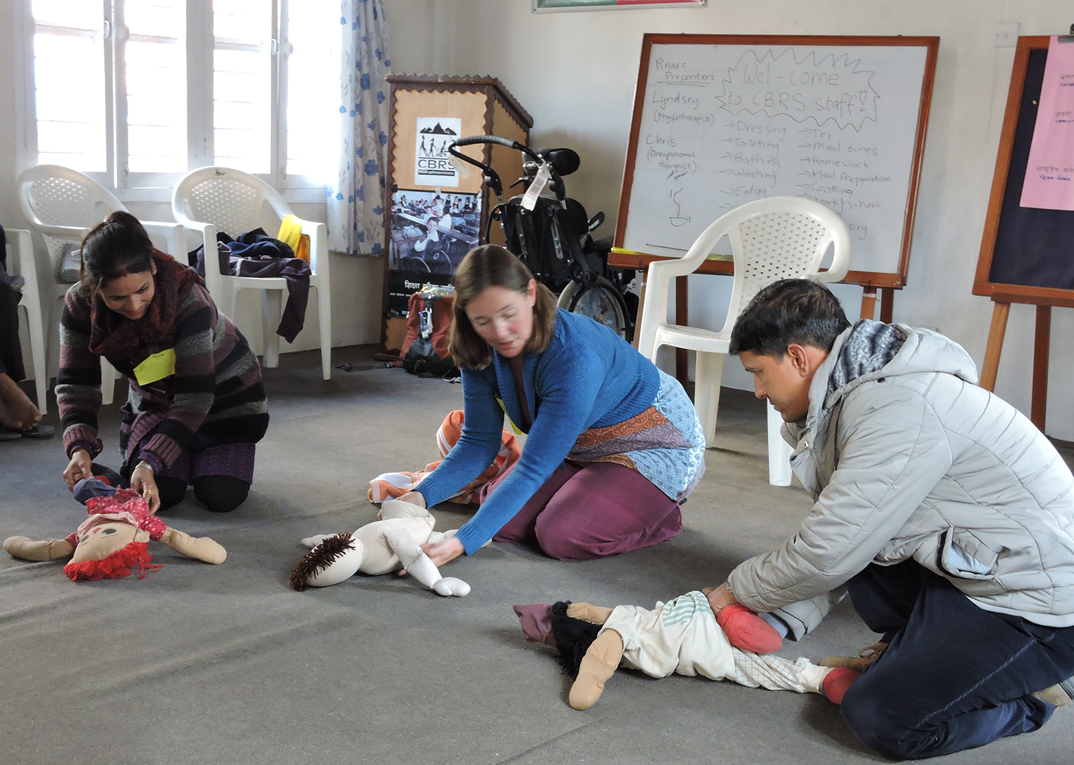 A health volunteer demonstrating physiotherapy techniques on toddler sized dolls with Nepali Health workers